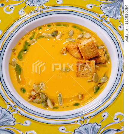 Vibrant pumpkin soup with croutons in decorative bowl 115930364