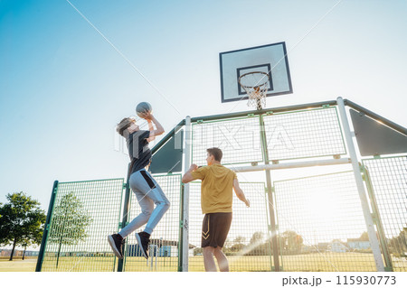 Two Young Caucasian Men Playing Basketball at the Park outdoor playground in sunset light. Teenagers' hobby, offline activity. Concept of sports, hobbies and healthy lifestyle. Selective focus. Two Young Caucasian Men Playing Basketball at the Park outdoor playground in sunset light. Teenagers' hobby, offline activity. Concept of sports, hobbies and healthy lifestyle. Selective focus. 115930773