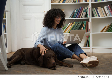 Curly-haired woman with laptop sitting on the floor, a dog next to her Curly-haired woman with laptop sitting on the floor, a dog next to her 115933523