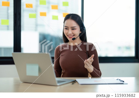 Smiling Call Center Agent with Headset Working on Laptop in Modern Office with Sticky Notes on Glass Wall Smiling Call Center Agent with Headset Working on Laptop in Modern Office with Sticky Notes on Glass Wall 115933682