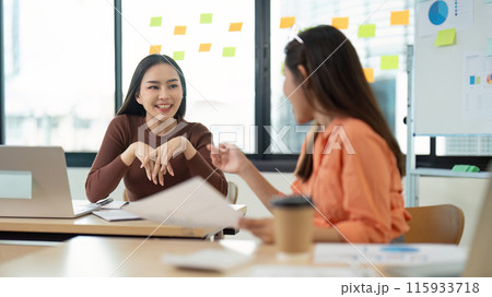 Two Young Women Collaborating in a Modern Office Setting with Laptops and Documents Two Young Women Collaborating in a Modern Office Setting with Laptops and Documents 115933718