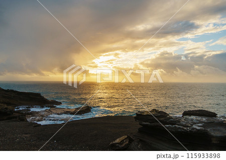 Beautiful sunset reflecting on calm water with rocks in foreground Beautiful sunset reflecting on calm water with rocks in foreground 115933898