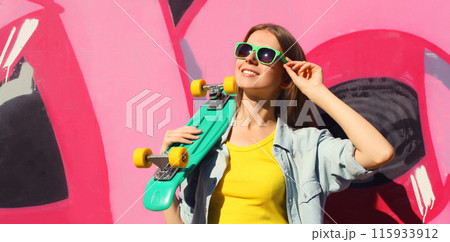 Stylish happy young girl with skateboard in glasses, modern teenager posing against on graffiti wall 115933912