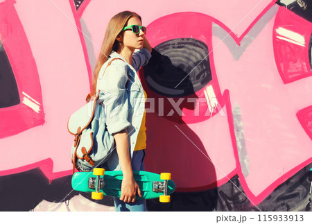 Stylish young girl with skateboard in glasses, modern teenager girl posing against the graffiti wall 115933913