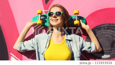 Stylish happy young girl with skateboard in glasses, modern teenager posing against on graffiti wall 115933916