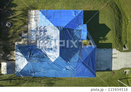 Aerial view of damaged in hurricane Ian house roof covered with blue protective tarp against rain water leaking until replacement of asphalt shingles 115934518