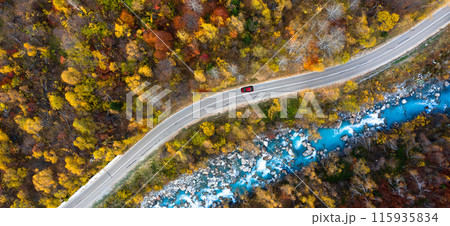 Aerial view of road and blue river with red car in fall forest in mountains. Top view 115935834