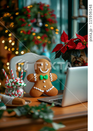 Christmas card with a gingerbread man near the laptop, the office is decorated with a wreath, on the table there is pot with poinsettia flower and a glass of candy canes, a wish for a Merry Christmas 115936148