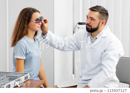 Doctor holding special eye equipment examinating girl's eyes in the ophthalmologic clinic Doctor holding special eye equipment examinating girl's eyes in the ophthalmologic clinic 115937127