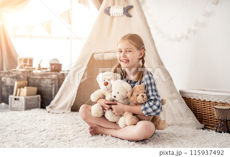 Happy little girl playing with teddy bears in room with wigwam in kids room Happy little girl playing with teddy bears in room with wigwam in kids room 115937492