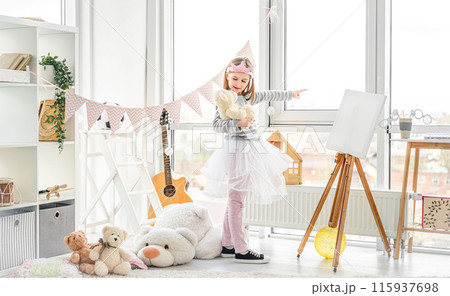 Cute little girl pointing at window for teddy bear in playroom Cute little girl pointing at window for teddy bear in playroom 115937698