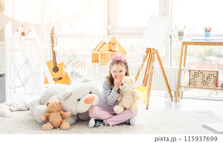 Happy little girl sharing secrets with teddy bear in light room 115937699