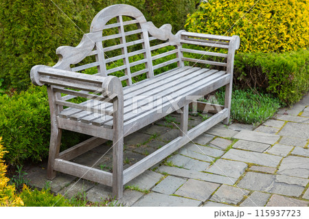 An empty vintage park bench stands on a paved ground 115937723