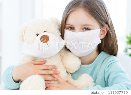 Little girl with plush teddy wearing medical masks at home Little girl with plush teddy wearing medical masks at home 115937730