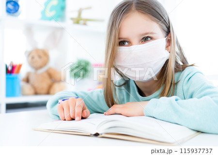 Beautiful little girl in medical mask reading book 115937737