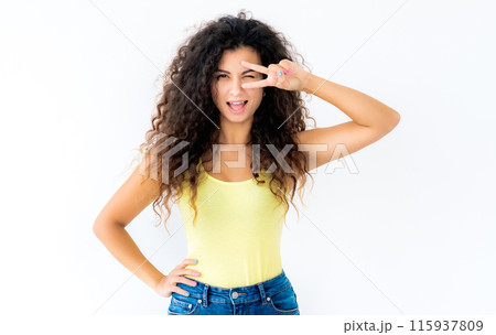 Beautiful curly girl making victory sign near her blinked eye Beautiful curly girl making victory sign near her blinked eye 115937809