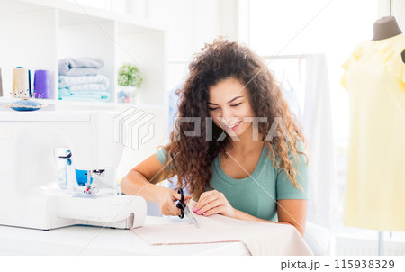 Cute needlewoman cutting fabric with scissors indoors Cute needlewoman cutting fabric with scissors indoors 115938329