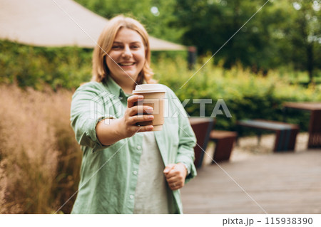Coffee to go at autumn park. Food, rest, Take away concept. Place logo on mug, mockup. Woman hand holding brown paper cup on park background Coffee to go at autumn park. Food, rest, Take away concept. Place logo on mug, mockup. Woman hand holding brown paper cup on park background 115938390