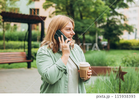 Happy cheerful young woman in fashion clothes talking on Phone with eco cup of tea. Mockup, Woman holding smartphone and coffee cup in city park. Urban, drinks and people concept. High quality photo Happy cheerful young woman in fashion clothes talking on Phone with eco cup of tea. Mockup, Woman holding smartphone and coffee cup in city park. Urban, drinks and people concept. High quality photo 115938393
