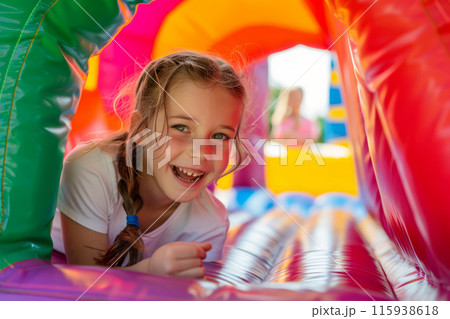Joyful girl playing inside a vibrant colorful bounce house. Happiness and fun Joyful girl playing inside a vibrant colorful bounce house. Happiness and fun 115938618