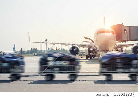 Luggage motion blurred trolley cart going fast delivering passenger baggage to modern plane on taxiway at airport on bright sunny day. Commercial aircraft on background at sunset or sunrise time 115938837