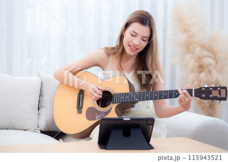 Young asian woman sitting on sofa looking tablet for practice music with guitar in living room. Young asian woman sitting on sofa looking tablet for practice music with guitar in living room. 115943521