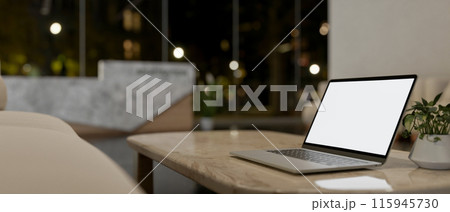 A laptop computer on a neutral marble coffee table in a modern lobby lounge at night. 115945730