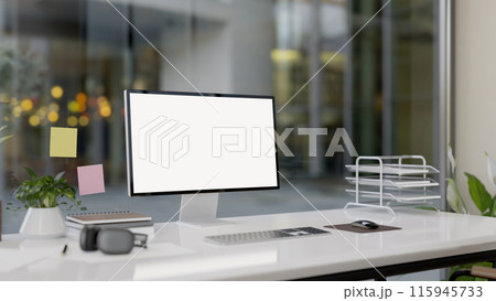 A modern office features a computer with a white-screen mockup and office supplies on a white desk. 115945733