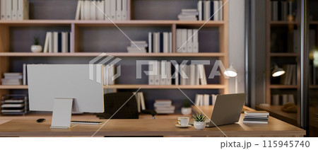 A contemporary luxurious private office at night features a computer and a laptop on a table. A contemporary luxurious private office at night features a computer and a laptop on a table. 115945740