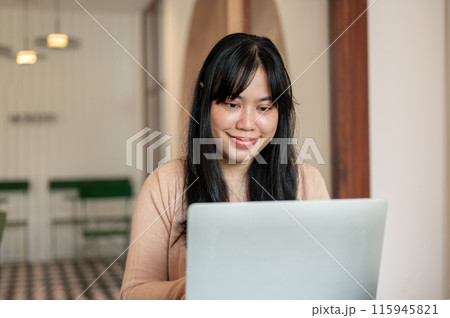 A charming, positive Asian woman is working remotely from a coffee shop, working on her laptop. A charming, positive Asian woman is working remotely from a coffee shop, working on her laptop. 115945821