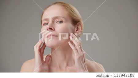 Anti age, Beauty, health and dry skin care concept - beautiful middle-aged mature Caucasian woman in her 50s touching her face skin and looking at the camera with a slight smile 115948109