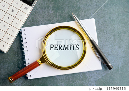 Business concept. The text PERMITS. through a magnifying glass in a notebook on a gray background 115949516