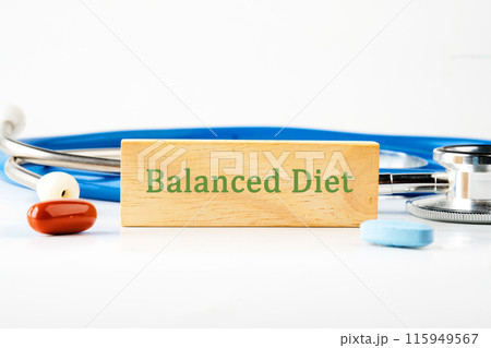 Balanced Diet text written on a wooden bar in front of a stethoscope next to pills, vitamins 115949567