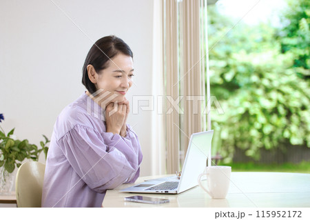 リビングでコーヒーを飲みながらパソコンを見るミドル女性 115952172