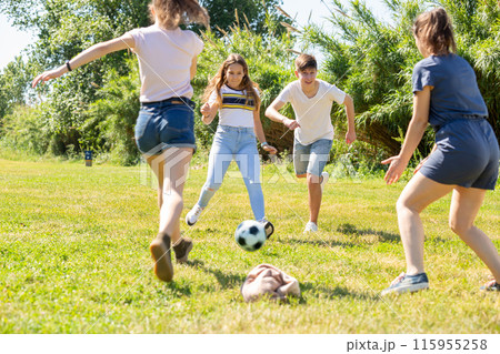 Happy teenage girls and guy playing football on lawn Happy teenage girls and guy playing football on lawn 115955258