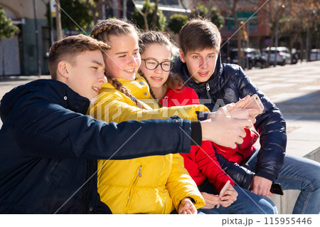 Four young happy teenagers taking self picture using mobile phone outdoors 115955446