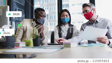 Image of social media icons over diverse colleagues wearing face masks discussing at office 115955923