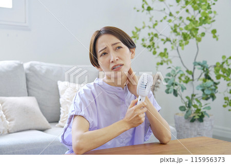 蒸し暑いリビングで携帯扇風機を使う女性 115956373