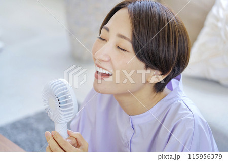 リビングで携帯扇風機を使う女性 リビングで携帯扇風機を使う女性 115956379