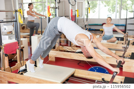 Young guy doing full body exercises lying on reformer device Young guy doing full body exercises lying on reformer device 115956502