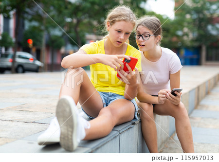Teenager girls using smartphones while sitting in park 115957013