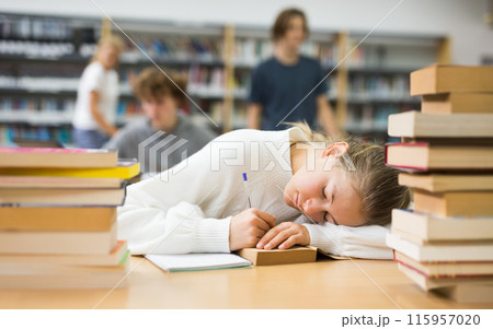 Tired girl fell asleep at table with textbooks in school library 115957020
