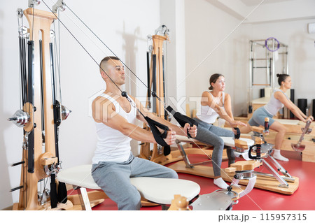 Sportive young guy training her arms pulling handle of cable exercise machine 115957315