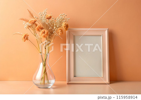 Wooden frame mockup on table against wall background in Pantone color 13-1023 Peach Fuzz with vase of dried flowers 115958914