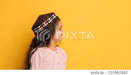 A child in a Turkic skullcap in front of a yellow background 115962882