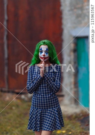 Portrait of a greenhaired girl in chekered dress with joker makeup on a rusty metal wall background. 115963567