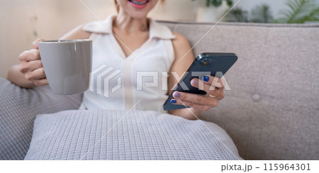 Woman Enjoying Social Media at Home with Coffee, Relax on Sofa, Smiling and Engaged with Smartphone 115964301