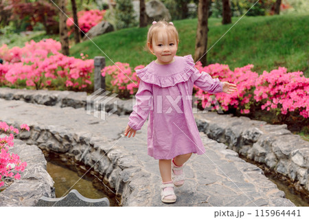Child girl in pink dress walking in summer blooming garden 115964441