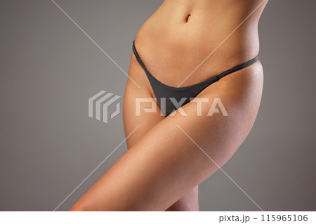 Close-up of woman's lower torso in black underwear, showcasing her slim and toned body against warm grey studio background. Close-up of woman's lower torso in black underwear, showcasing her slim and toned body against warm grey studio background. 115965106