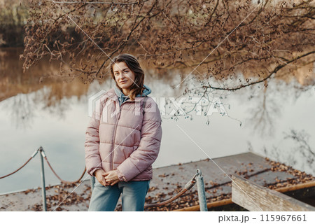 A young woman standing at the shore looking at the river in autumn sunny day. Street view, copy space for text, travel photo. Happy tourist woman on the bank of the river in autumn in warm clothes A young woman standing at the shore looking at the river in autumn sunny day. Street view, copy space for text, travel photo. Happy tourist woman on the bank of the river in autumn in warm clothes 115967661